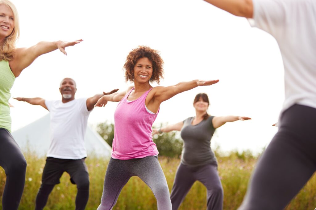 Female Teacher Leading Group Of Mature Men And Women In Class At Outdoor Yoga Retreat