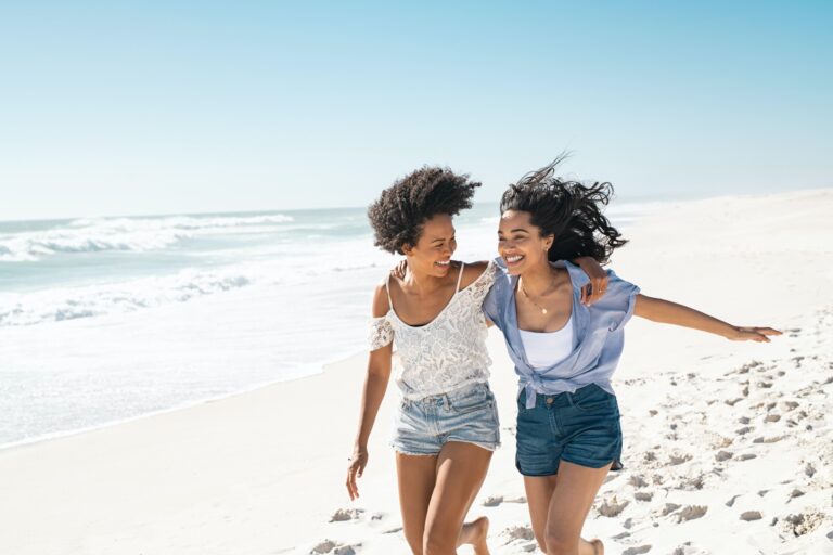 Happy women friends running on summer beach with copy space