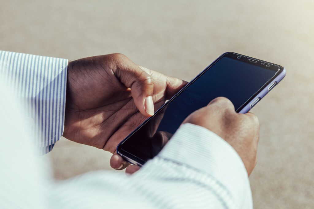 Very close-up view of afro hands using mobile phone outdoors.